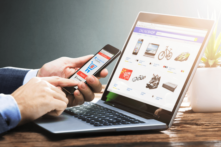 ecommerce website on computer with person holding phone with shopping cart